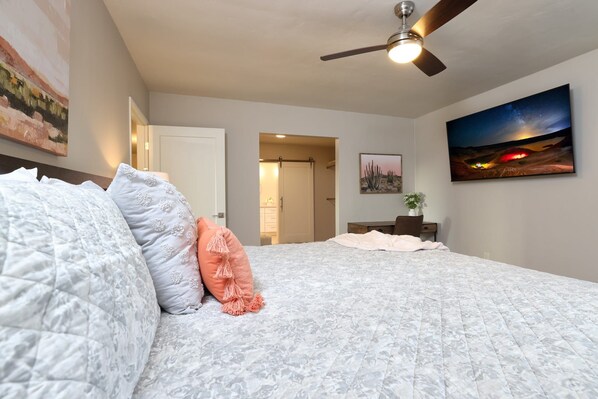 A bedroom with a bed, a ceiling fan, a night sky painting, and a desert landscape painting. - Tierra Velo - HGTV Style in East Tucson (Tucson)