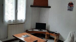 Huoneessa on puinen pöytä, televisio, patteri ja ikkuna, jossa on verhot.