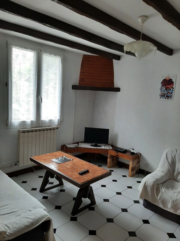 A room with a wooden table, a television, a radiator, and a window with curtains.