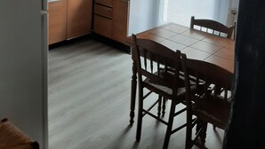 Keittiössä on puukehikoiset kaapit, ruokapöytä tuoleineen, jääkaappi ja kattotuuletin.