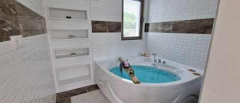 Un baño moderno con una bañera independiente, paredes de azulejos blancos y un ventanal.