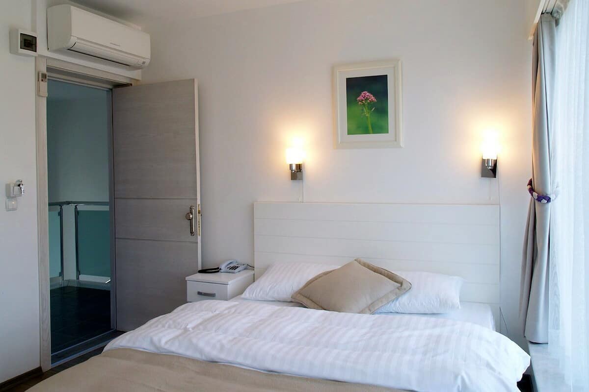 A hotel room with a bed, bedside table, and a wall-mounted air conditioner.