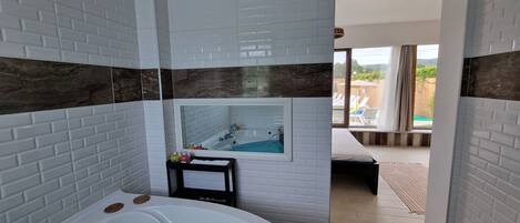 A bathroom with a large bathtub, a mirror, and a view of a pool area.