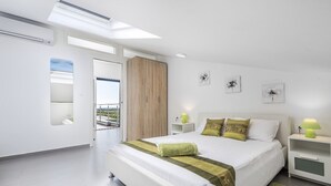 Une chambre moderne avec un grand lit, une lucarne, une vue sur l’extérieur et une petite table de chevet avec une lampe.