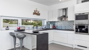 Une cuisine moderne avec des meubles blancs, un plan de travail noir et une fenêtre donnant sur un espace verdoyant.