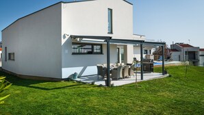 Une maison moderne dotée d’un patio couvert, d’une piscine et d’une pelouse bien entretenue.