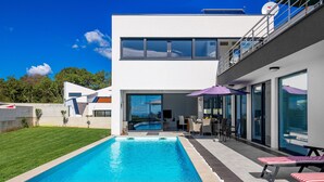Une maison moderne dotée d’une piscine, d’un espace salon extérieur et d’un balcon.