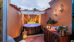 A cozy outdoor patio with a hot tub, a wooden table with candles, and decorative wall sconces.