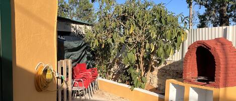 Un patio con horno de ladrillo, mobiliario exterior y pared amarilla.