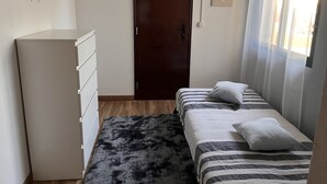 Une chambre à coucher avec un lit, une commode, une porte et une fenêtre avec des rideaux.