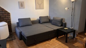 Un espace de vie compact comprenant un canapé-lit, une petite table, une lampe sur pied et un radiateur.