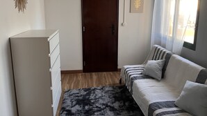Une pièce avec une porte en bois, une commode blanche, un canapé avec des coussins à rayures et une œuvre d’art représentant une feuille, encadrée, accrochée au mur.