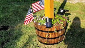 A wooden post with the number 465, a small American flag, and a solar-powered light fixture on a grassy lawn. - Perfectly centered in the Birch Harbor Village! (Birch Harbor)