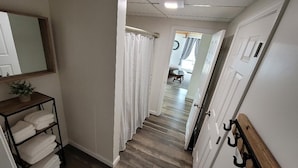 A hallway with a wooden floor, a white door with a coat rack, and a shelf with folded towels. - Perfectly centered in the Birch Harbor Village! (Birch Harbor)