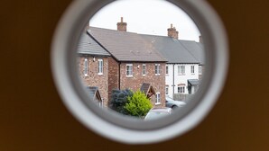 A view through a circular window of a row of brick houses with a car parked in the driveway. - Superb space in the idyllic village of Loppington - Pass the keys (Shrewsbury)