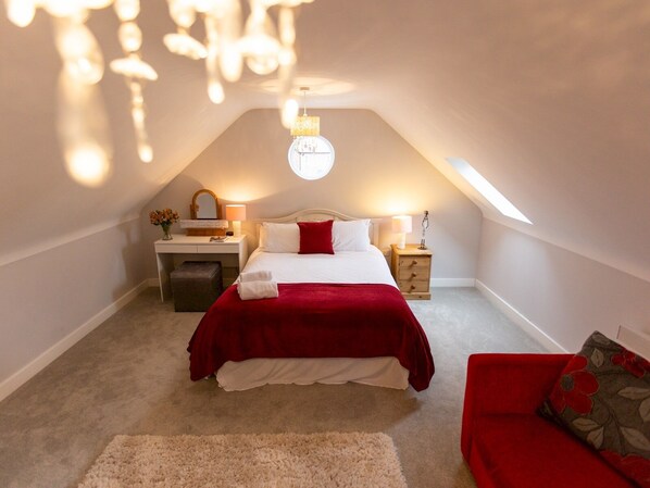 A bedroom with a bed, bedside tables, a nightstand, a mirror, a chandelier, and a red sofa.