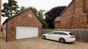 A white car parked in a brick driveway with a garage and a wooden fence. - Superb space in the idyllic village of Loppington - Pass the keys (Shrewsbury)