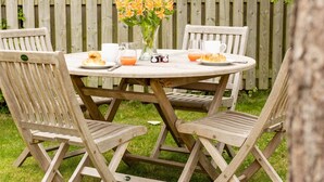 A round wooden table with a white tablecloth, surrounded by four wooden chairs with a cross-back design. A vase with flowers is placed on the table, and there are plates with food and drinks. - Superb space in the idyllic village of Loppington - Pass the keys (Shrewsbury)