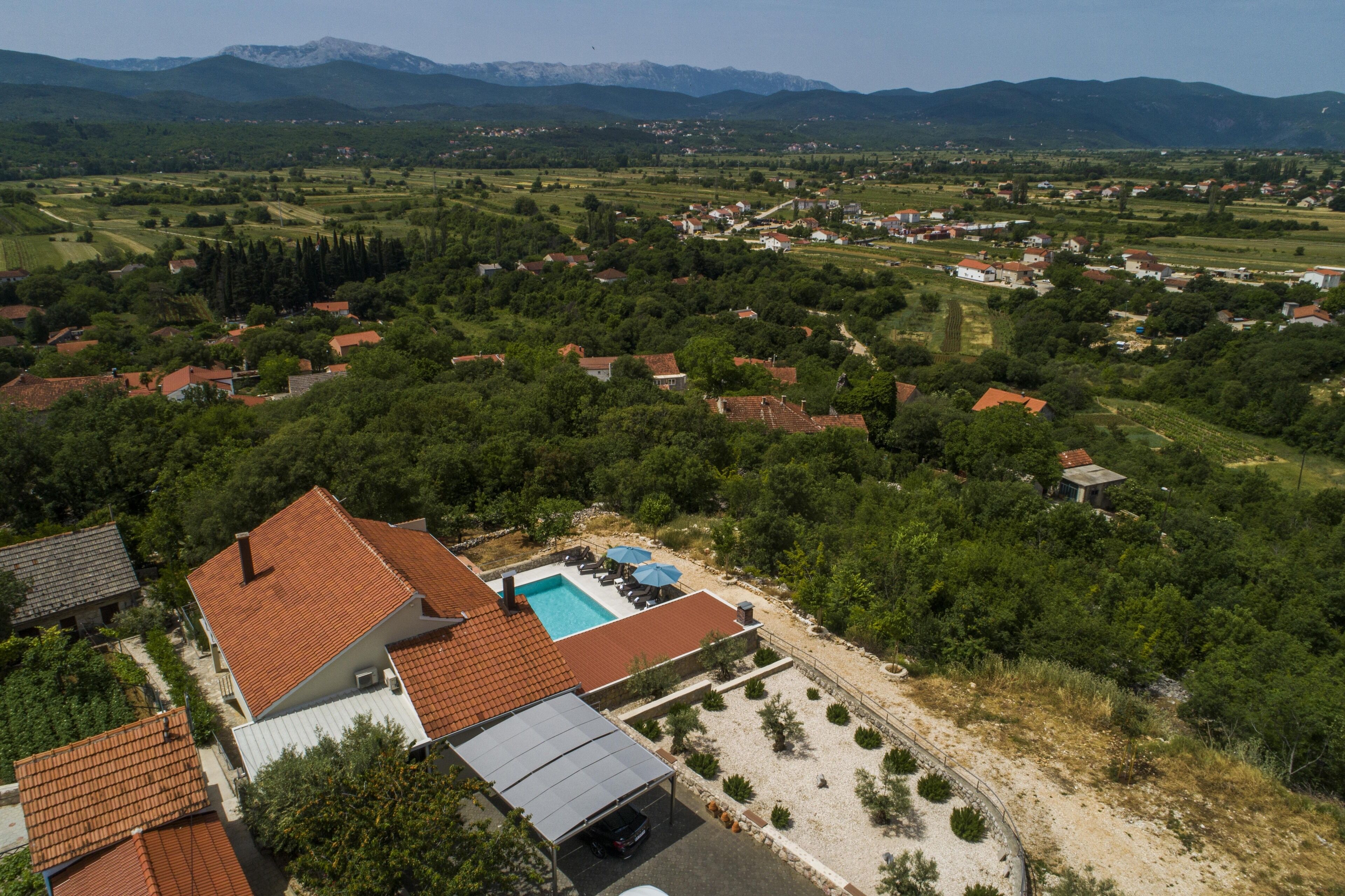 Zona residencial con piscina, rodeada de casas y vegetación, con montañas al fondo.