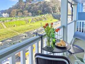 Un balcon avec une table, un vase rempli de fleurs et une assiette de pâtisseries.