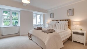 A bedroom with a large bed, bedside tables, a radiator, and a window with a view of greenery.