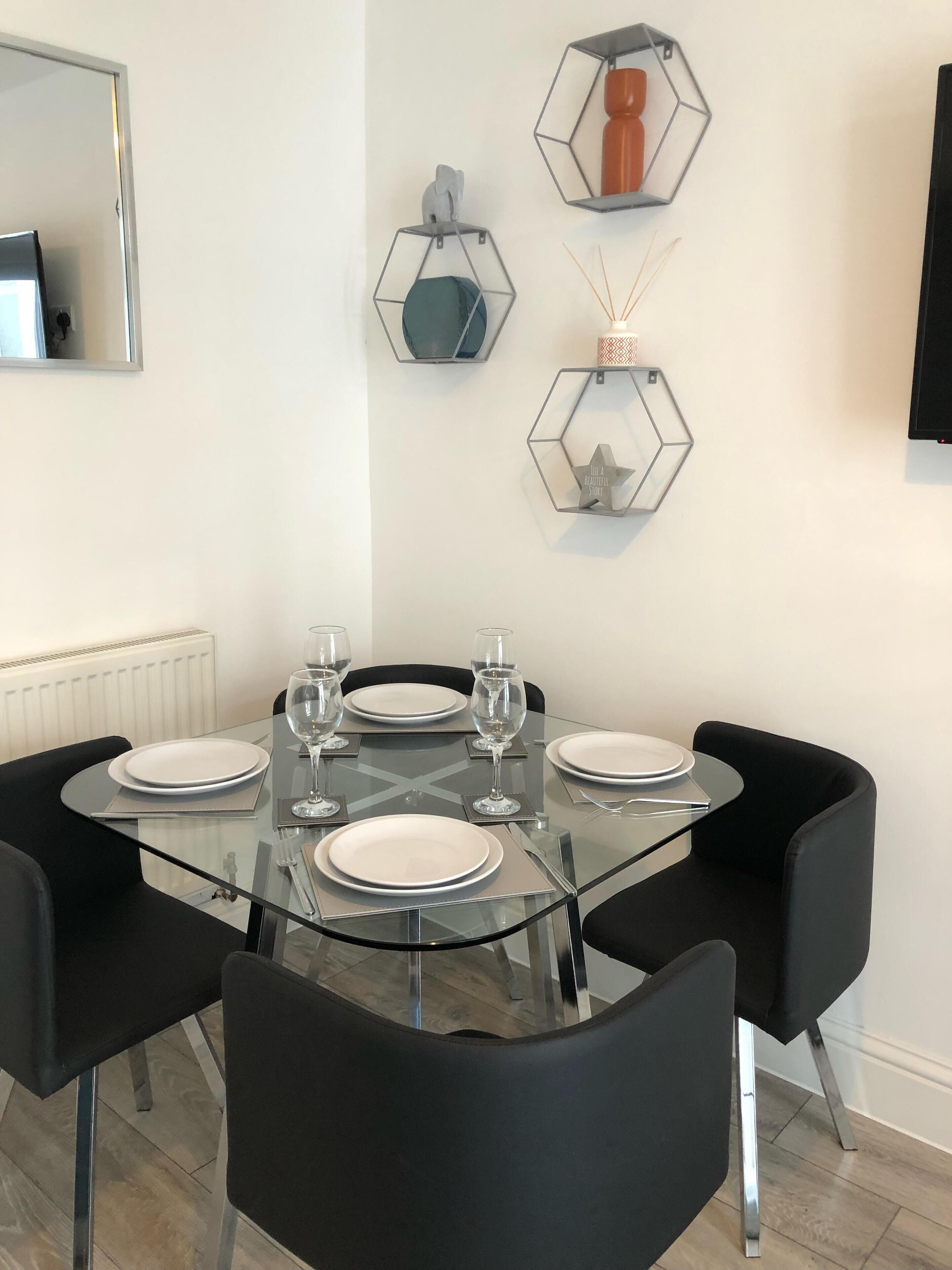 A dining area with a glass table set for four, surrounded by black chairs.