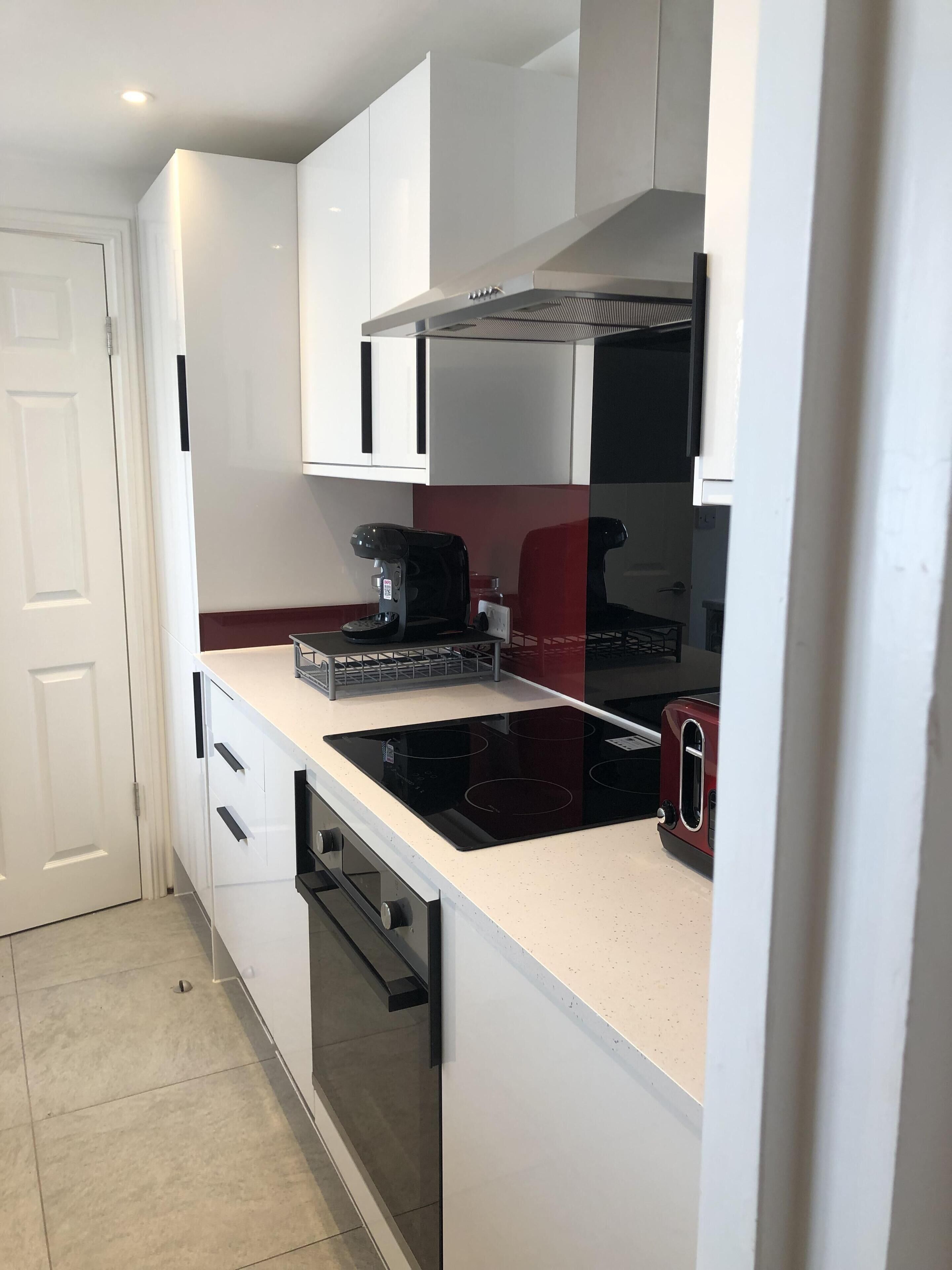 Una cocina compacta con armarios blancos, una estufa negra y un tostador rojo.
