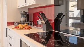 Eine moderne Küche mit einer schwarzen Kochplatte, einer Kaffeemaschine, einem Schneidebrett mit Erdbeeren und Croissants sowie einem Messerblock.