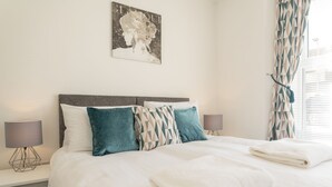 Ein ordentlich bezogenes Bett mit weißer Decke und zwei Kissen, einer Nachttischlampe und einem Wandbild.