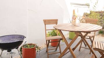 A wooden outdoor table and chairs, a grill, and potted plants on a wooden deck.