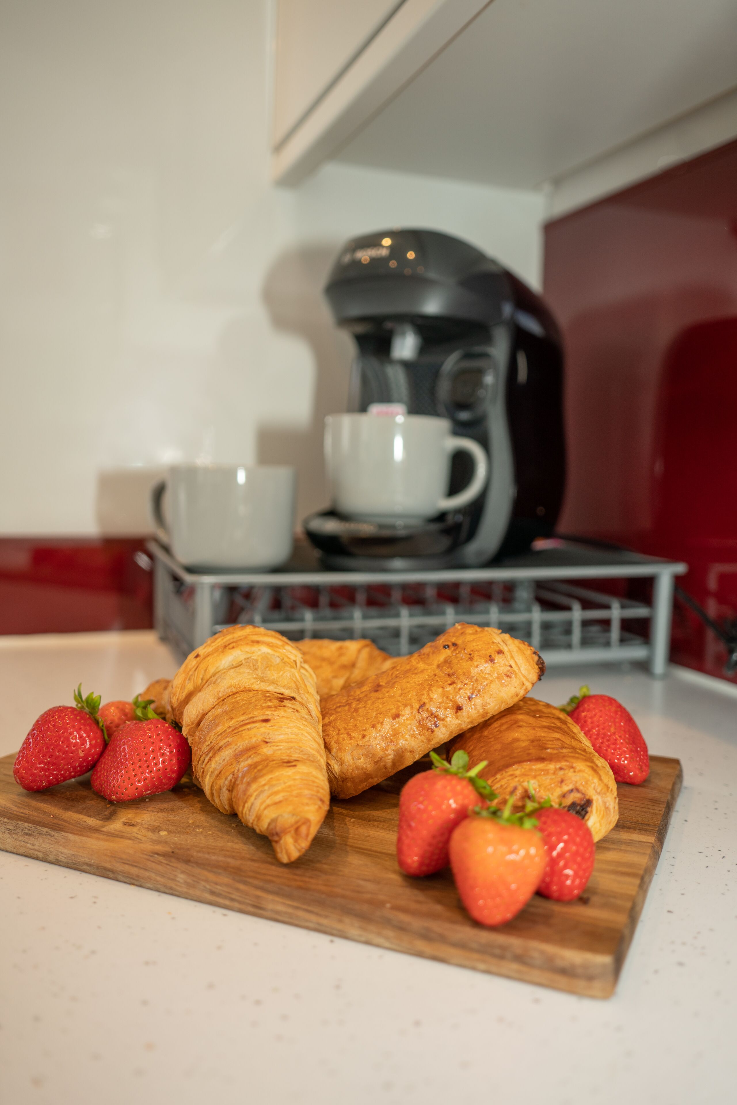 Una tabla de madera con croissants y fresas sobre una encimera de cocina.