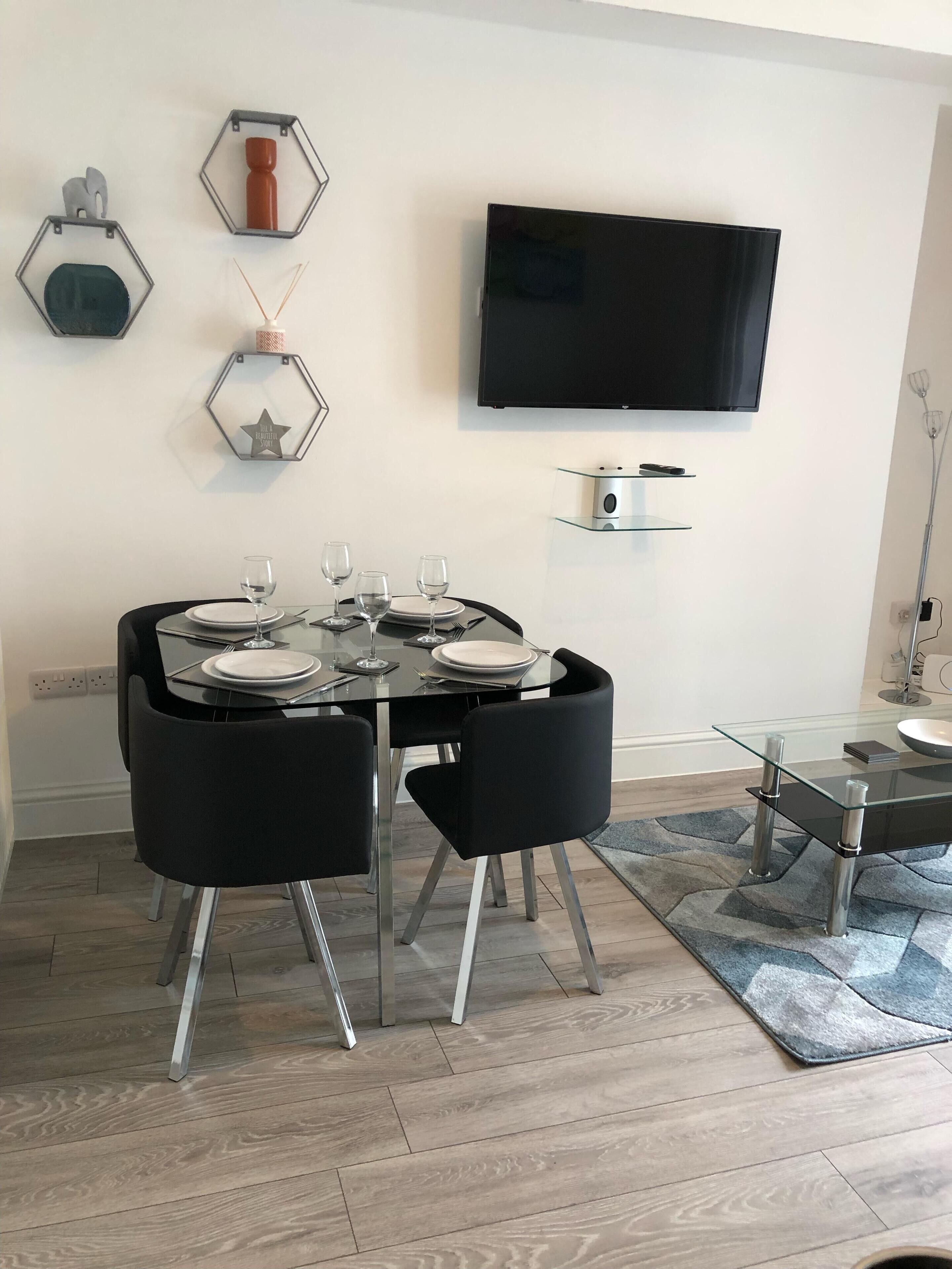 A modern dining area with a glass table, black chairs, and a mounted TV.