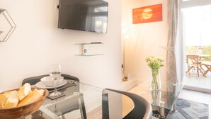 Ein moderner Essbereich mit einem Glastisch, Stühlen und einer Schüssel mit Brot. Ein Flachbildfernseher ist an der Wand über dem Tisch befestigt.