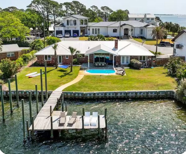 A waterfront property with a dock, a swimming pool, and a large house with a garage.
