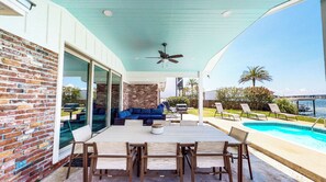 A covered patio with a pool, a blue sofa, and a dining table with chairs.