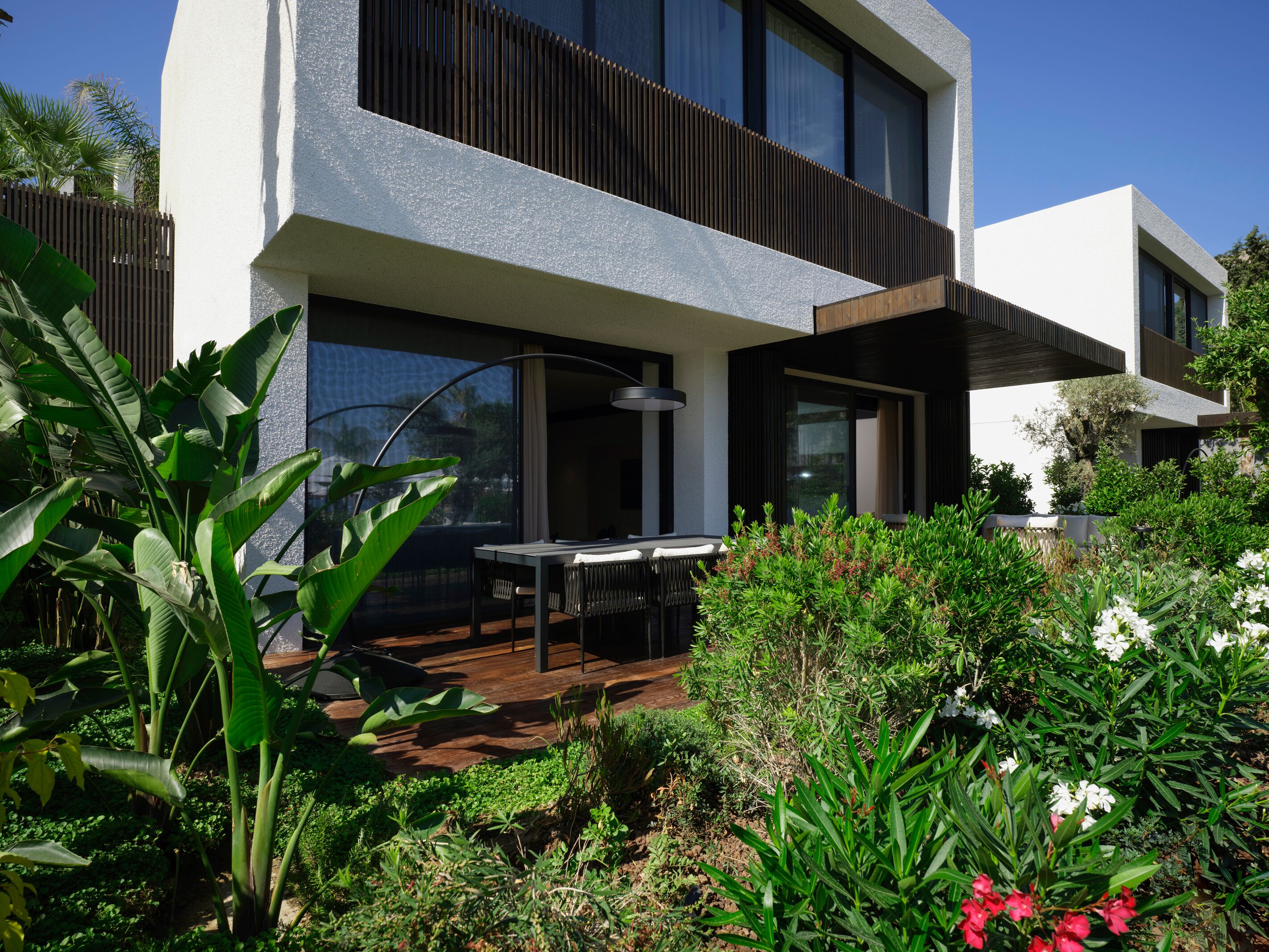 Une maison moderne dotée d’un patio, de grandes fenêtres et d’une végétation luxuriante.