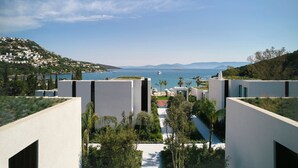 Un hotel frente al mar con arquitectura moderna, un camino que lleva a la playa y vistas al océano y montañas distantes.
