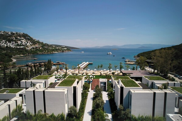 Un hotel costero de arquitectura moderna, un puerto deportivo y vistas al mar.