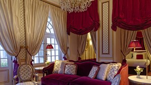Una habitación lujosa con un sofá de terciopelo rojo y elegante, cortinas ornamentadas y muebles clásicos.