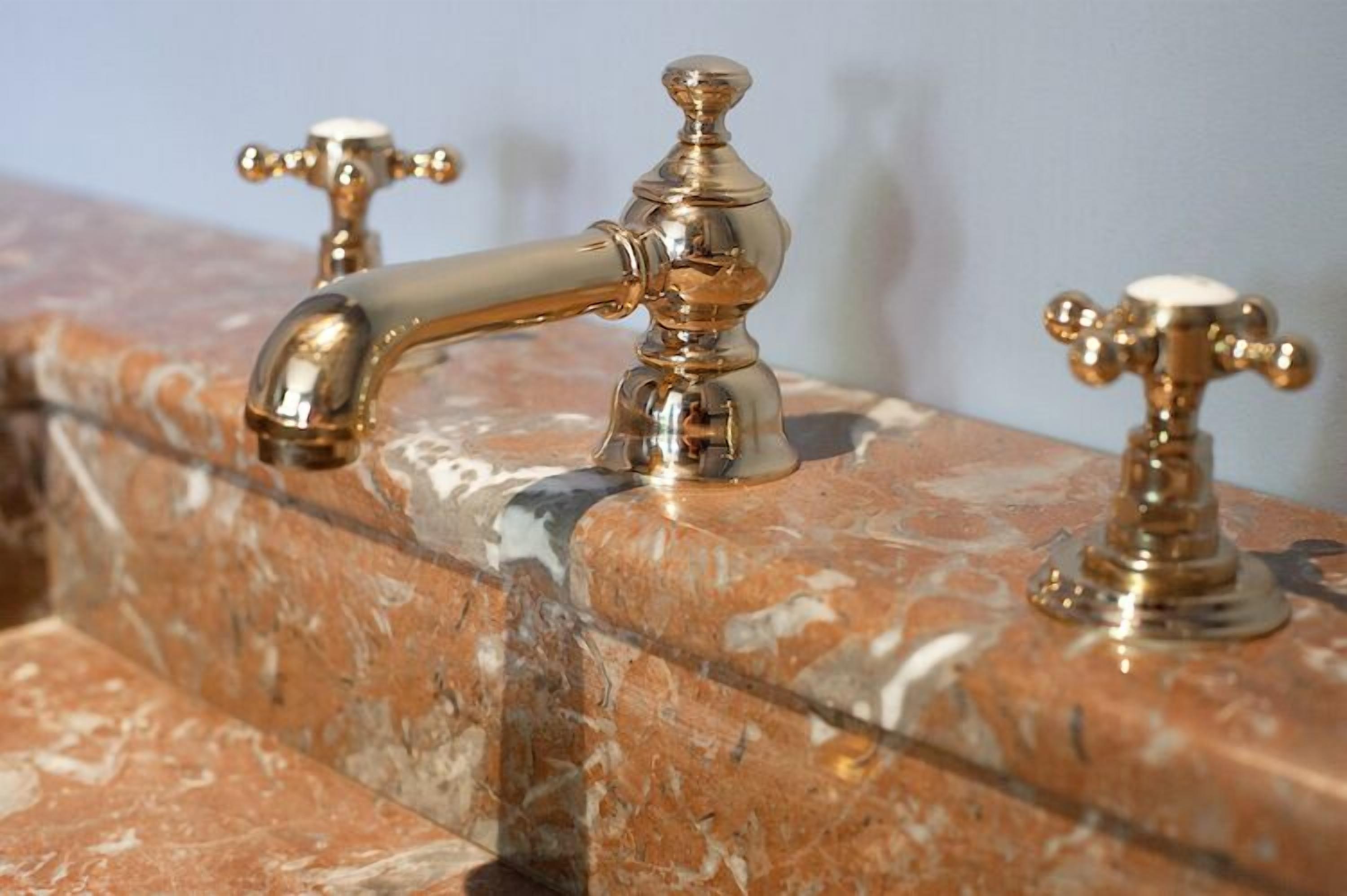 A marble sink with three gold faucets.