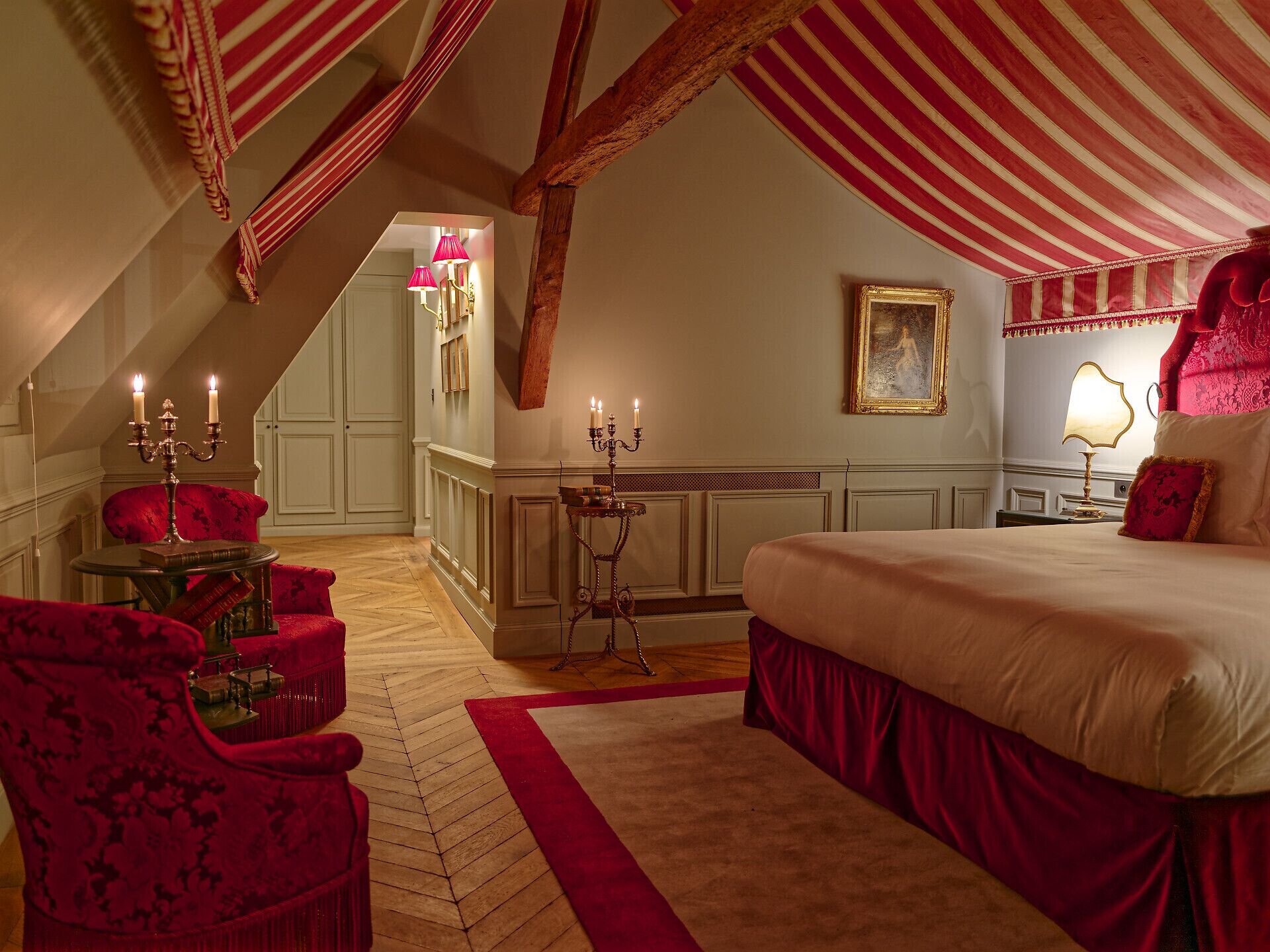 A bedroom with a large bed, a red and white striped ceiling, and a chandelier.