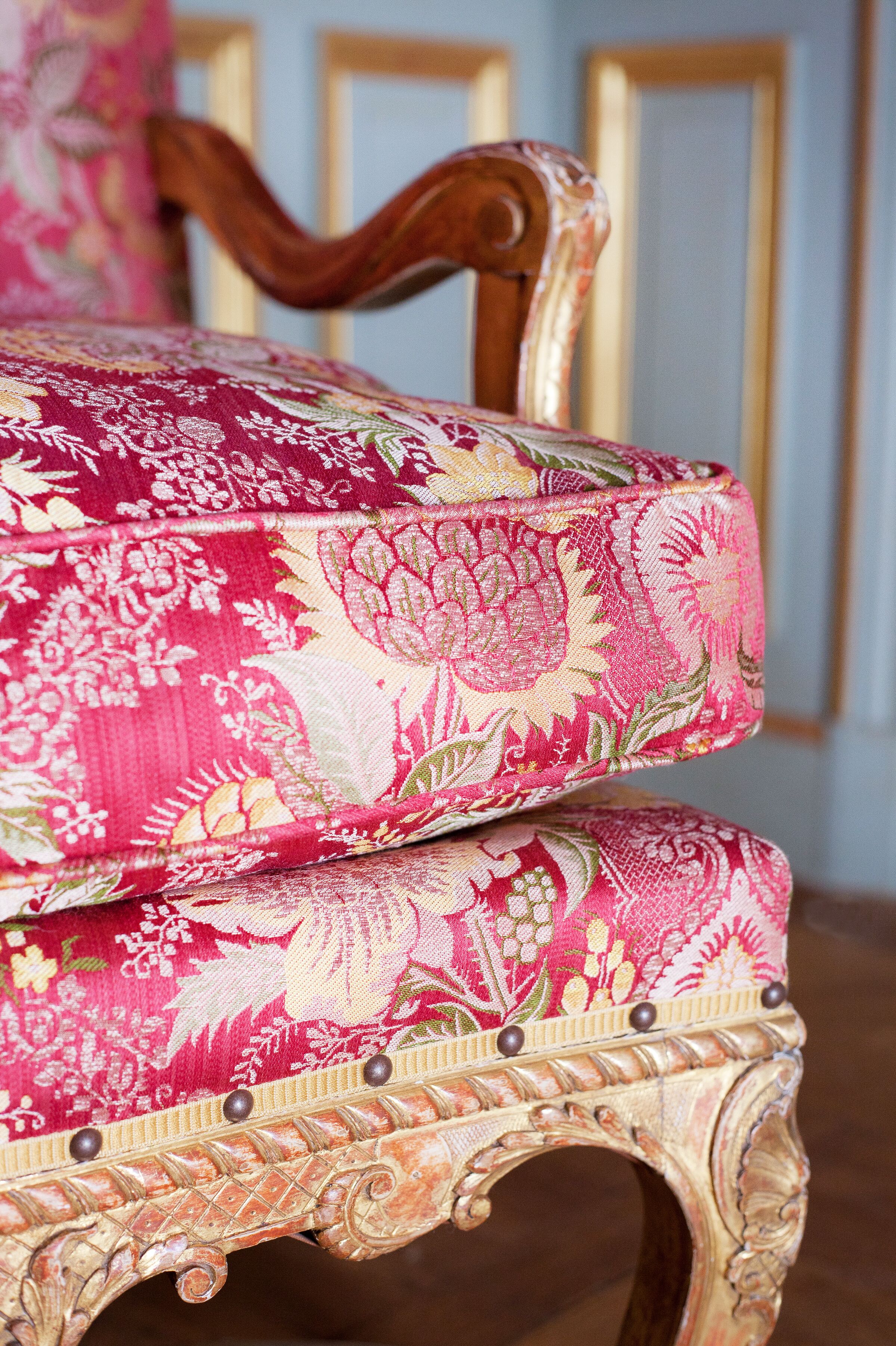 Een stoel met versierde houten details en een stoffen bekleding met bloemenmotief.