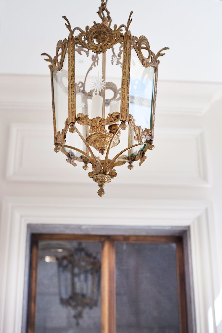 Um lustre ornamentado com detalhes elaborados, pendurado em um quarto com uma porta branca e uma janela com vista.