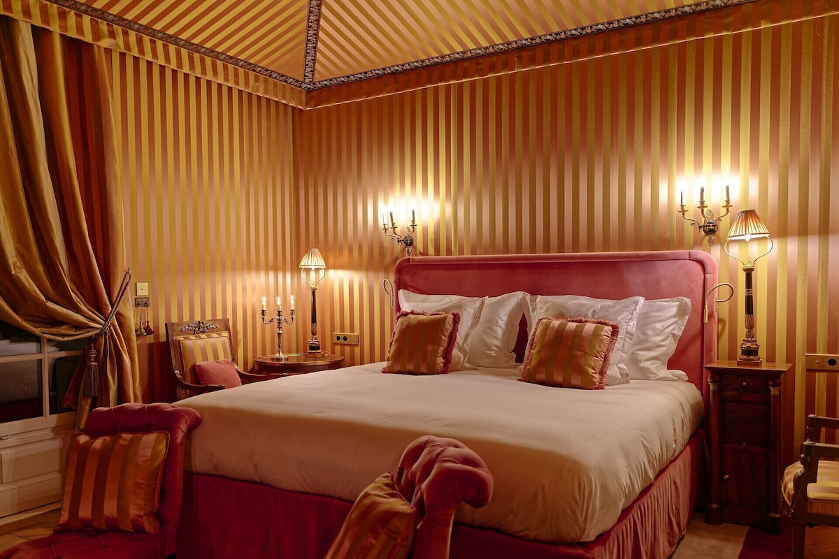 Un grand lit avec une tête de lit rouge, deux tables de chevet avec des lampes et un fauteuil rouge.