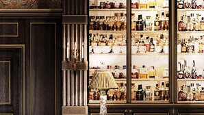 Zona de bar con paneles de madera oscura, una barra acolchada en tonos verde y una exhibición de diferentes botellas.