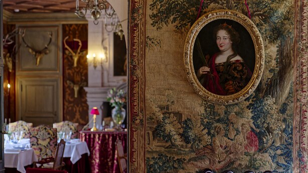 Una habitación con decoración elaborada, que incluye un tapiz, un retrato enmarcado y una araña.
