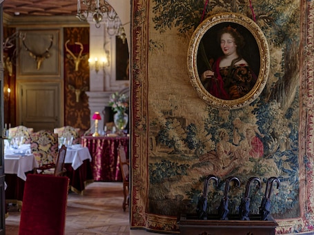 A room with ornate decor, including a tapestry, a framed portrait, and a chandelier.