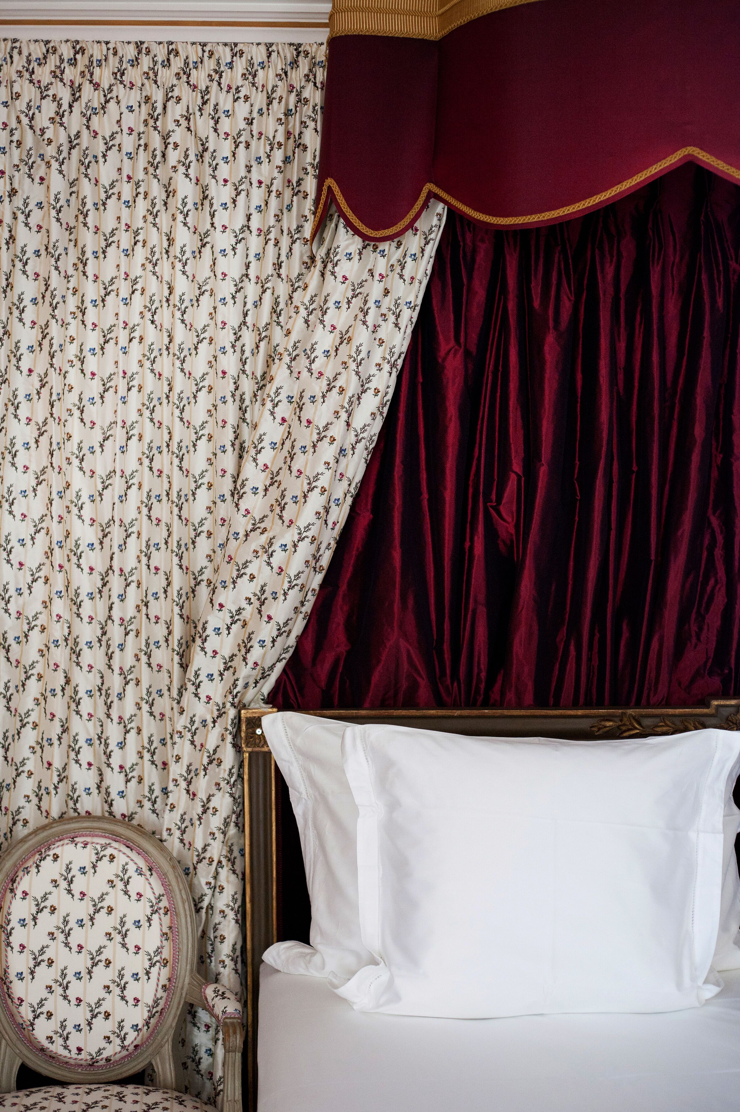 Un dormitorio con cama, una silla y cortinas.