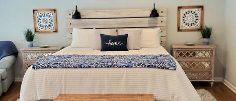 Ein Schlafzimmer mit einem Bett, einem Deckenventilator, einem Nachttisch mit einer Lampe und einem Beistelltisch mit einer Pflanze.