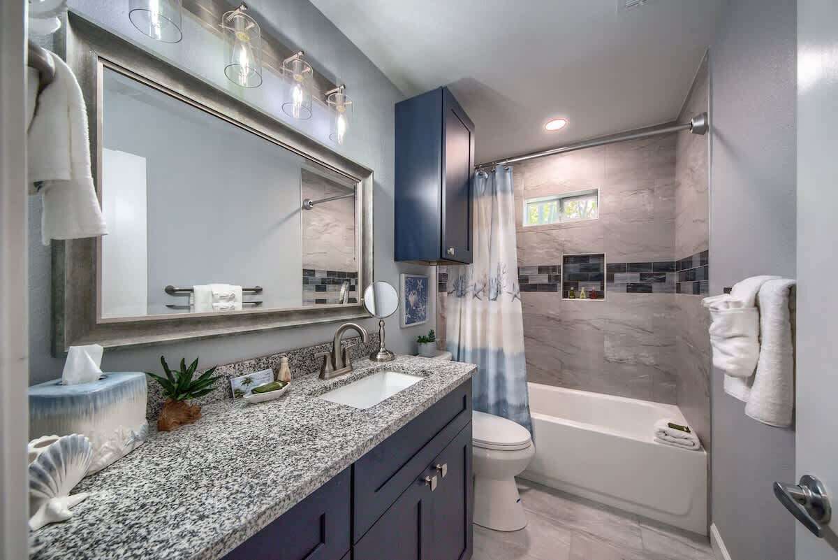 Een moderne badkamer met een granieten aanrechtblad, een grote spiegel, een badkuip en een douchegordijn.